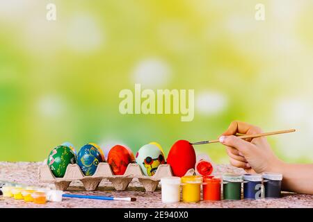 Bunte Ostereier in einem Neststand werden von weiblicher Hand mit hellen Akril-Farben auf grünem Hintergrund bemalt. Rote traditionelle Osterei Stockfoto