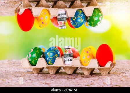 Spiegelbild von pascal gefärbten Eiern in der Nähe einer Ampulle mit Covid 19-Impfstoff auf einem Karton. Grün beleuchtender Hintergrund. Pascal Urlaub während einer Stockfoto