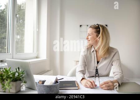Die blonde, schöne Architektin sitzt in ihrem Büro und träumt von besseren Zeiten ohne Corona Stockfoto
