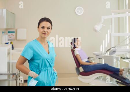 Lächelnde Frau Arzt Zahnarzt Blick auf Kamera über sitzende Frau Patient im Hintergrund Stockfoto