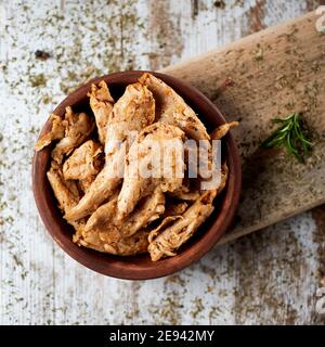 Hochwinkelansicht von einigen gekochten Hühnerfleisch Streifen in einer Steingutschüssel, auf einem rustikalen Holztisch, in einem quadratischen Format platziert Stockfoto