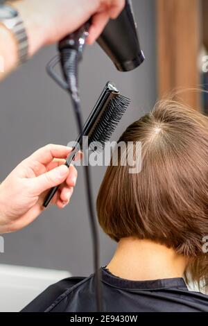 Friseur trocknet braune Haare der jungen Frau in einem Schönheitssalon Stockfoto