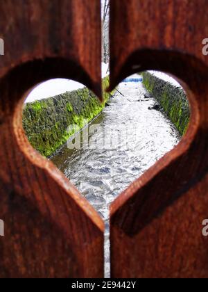 Vertikale Aufnahme eines strömenden Kanals durch ein herzförmiges Loch Auf einer hölzernen Oberfläche Stockfoto