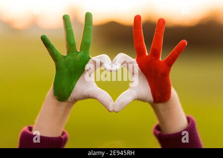 Herz Form von Kindern handbemalt in italien Flagge Farben, Kinder Körpersprache, Kinder Liebe Konzept. Herz Hand auf Natur Sonnenuntergang Bokeh Hintergrund Stockfoto