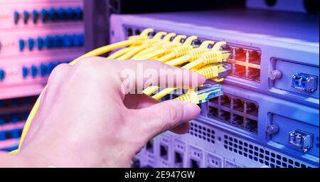 Hand, die Netzwerkkabel auf dem Switch Hub im Server raum Hintergrund Stockfoto
