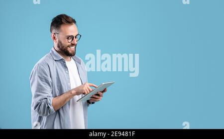 Smart Millennial Kerl in Brille mit Tablet-Computer über blauen Studio-Hintergrund, Banner-Design mit Kopierraum Stockfoto