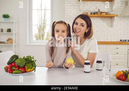 Glückliche Mutter und Tochter am Küchentisch mit Obst, Gemüse und Nahrungsergänzungsmitteln Stockfoto