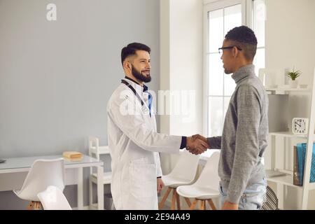 Lächelnder junger Arzt begrüßt neuen Patienten in seinem Büro Die Klinik oder das Krankenhaus Stockfoto