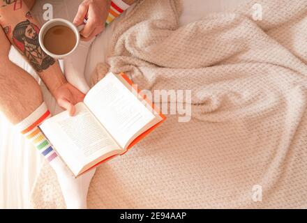 Mann trinkt Kaffee und liest morgens ein Buch im Bett. Rest-Konzept. Stockfoto