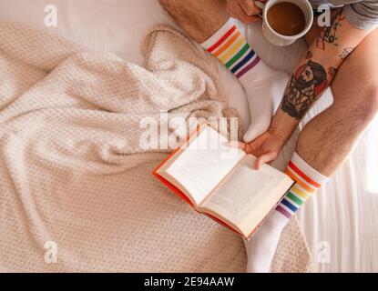 Ruhe und Menschen Konzept - Nahaufnahme von Menschenbeinen mit einem Buch trinken Kaffee im Bett zu Hause am Morgen. Stockfoto