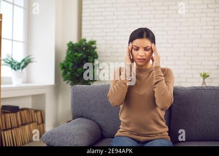 Gestresste junge Frau, die ihre Schläfen reibt, an schweren Kopfschmerzen oder Migräne leidet Stockfoto