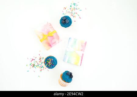 Süße Muffins, Süßigkeiten Konfetti und Regenbogen Geschenkbox auf weißem Hintergrund. Flach liegend, Draufsicht Stockfoto