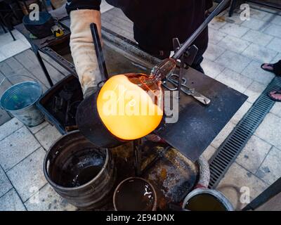 Handwerkliche Hände bilden das rote formbare Glas auf Glasbläserpfeife. Traditionelle Glasformtechnik. Handgemachtes Glasstudio in Kunratice. Stockfoto