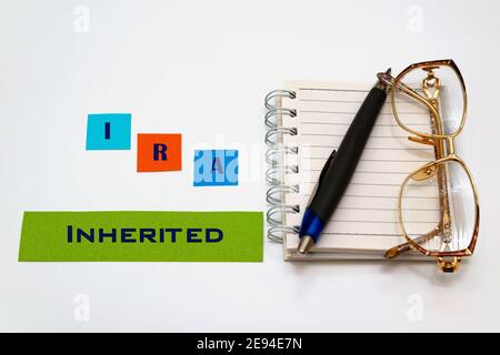 IRA erbte Text auf bunten Stickern, neben einem Notizbuch, einer Brille und einem Stift. Weißer Hintergrund. Stockfoto