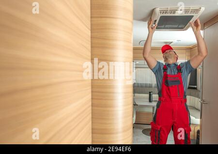RV-Servicemitarbeiter, der die an der Decke montierte Luftreinhalteeinheit für Reiseauflieger ersetzt oder repariert. Moderne Camper Technologien und Wartung. Stockfoto