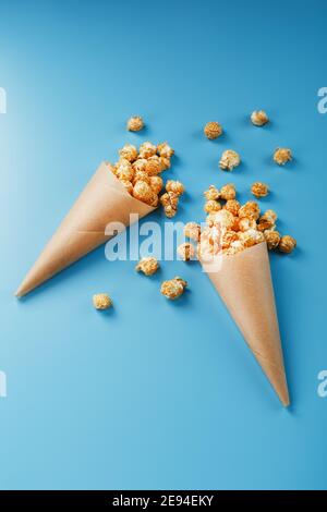 Karamell Popcorn in einem Papierumschlag auf blauem Hintergrund. Köstliches Lob für das Ansehen von Filmen, TV-Serien, Cartoons. Freier Speicherplatz, Nahaufnahme. Minimalisti Stockfoto