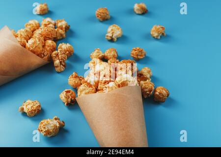 Karamell Popcorn in einem Papierumschlag auf blauem Hintergrund. Köstliches Lob für das Ansehen von Filmen, Serien, Cartoon. Freier Speicherplatz, Nahaufnahme. Minimalis Stockfoto