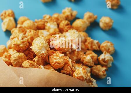 Karamell Popcorn in einem Papierumschlag auf blauem Hintergrund. Köstliches Lob für das Ansehen von Filmen, Serien, Cartoon. Freier Speicherplatz, Nahaufnahme. Minimalis Stockfoto