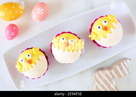 Schlüpfende Frühlingsküken Cupcakes auf einem Servierteller. Flay lag vor einem weißen Marmorhintergrund. Stockfoto