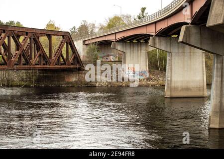 Beide Brücken liegen über dem Merrimack River in Hooksett, NH. Die alte rostige Brücke auf der linken Seite ist die Fußbrücke. Bekannt als Eisenbahnbrücke. Stockfoto