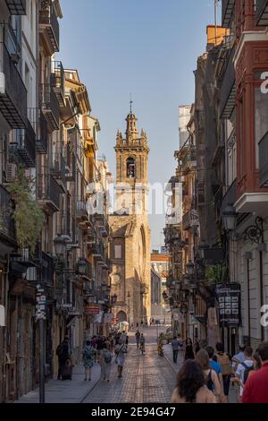 VALENCIA, SPANIEN - Jul 11, 2019: Vertikales Foto von Touristen und Einheimischen, die im Sommer in einer engen Straße mit einem Glockenturm im Hintergrund spazieren gehen Stockfoto