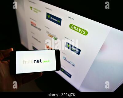 Person, die Mobiltelefon mit Logo des deutschen Telekommunikationsanbieters Freenet AG vor der Website mit Marken zeigt. Fokus auf Telefonbildschirm. Stockfoto