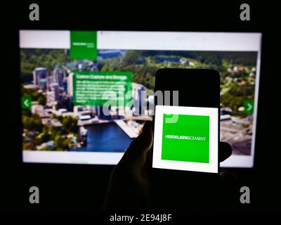 Person, die Smartphone mit Logo der HeidelbergCement AG vor der Website zeigt. Fokus auf Telefonbildschirm. Stockfoto