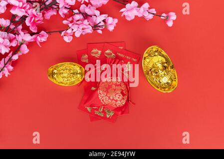 Chinesisches Neujahrskonzept - Sakura Blossom, rote Umschläge und goldenes Ingot auf rotem Hintergrund Stockfoto