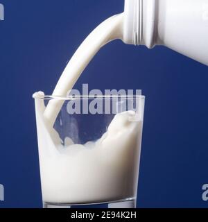 Gießen von Milch aus Plastikflasche in ein Glas auf blau Hintergrund Stockfoto