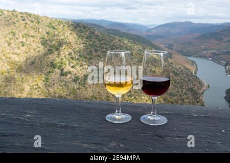 Gläser von portugiesischen angereicherten weißen und roten Portwein, in Douro-Tal und Douro Fluss mit bunten terrassenförmigen Weinbergen auf Hintergrund in au hergestellt Stockfoto