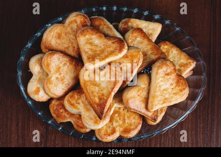 Hausgemachte herzförmige Kekse auf einem Glasteller auf einem Holzhintergrund mit Filmkorneffekt Stockfoto