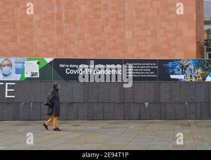 Eine Frau, die eine schützende Gesichtsmaske trägt, geht an einem Coronavirus-Informationsbanner am Francis Crick Institute in St. Pancras vorbei, während sie gesperrt wird. London, Großbritannien Februar 2021. Stockfoto