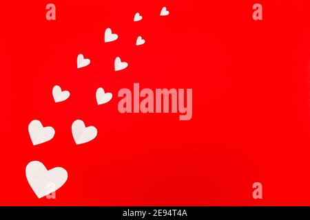 Komposition zum Valentinstag. Weiße Papierherzen auf rotem Hintergrund im flachen Lay-Stil. Valentinstag Konzept, Foto Vorlage Stockfoto