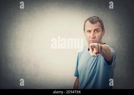 Selbstbewusster und entschlossener Mann mittleren Alters, der Zeigefinger zur Kamera zeigt, wie jemand beschuldigen oder beschuldigen, isoliert auf grauem Wandhintergrund mit Kopie sp Stockfoto