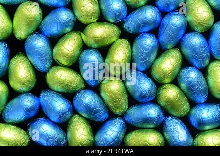 Stapel oder Gruppe von mehrfarbigen und verschiedenen Größen von bunten Folie verpackt Schokolade ostereier in blau, gelb und lindgrün. Stockfoto