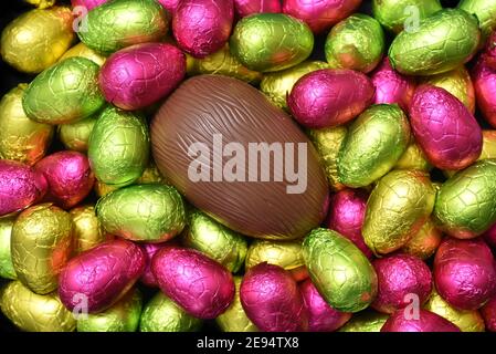 Stapel oder Gruppe von mehrfarbigen und verschiedenen Größen von bunten Folie verpackt Schokolade ostereier in rosa, rot, gelb und lindgrün. Stockfoto