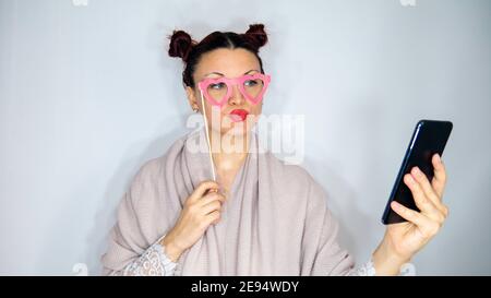 Frau mit rosa Herzbrille nutzt ihr Telefon für einen Videoanruf. Stockfoto