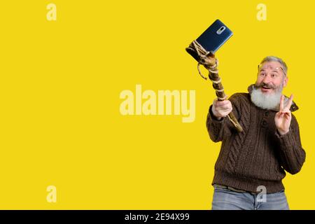 Studio Portrait von reifen bärtigen Mann Selfie mit Holzstab, lustige Selfie-Making-Konzept, gelber Hintergrund Stockfoto