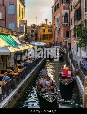 Venedig, Italien, 11. September 2020 – malerischer Kanal von Venedig mit Gondeln und Touristen auf der rechten Seite, die den Sonnenuntergang in einer Cocktailbar genießen Stockfoto