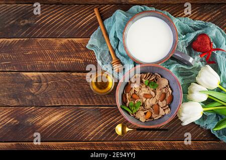 Dinkelflocken mit Milch zum Frühstück. Leichtes Frühstück am Valentinstag mit Tulpen und Herz Stockfoto