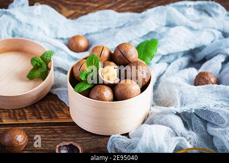 Macadamianüsse in Schale mit Minzblättern und Honig auf Holzhintergrund Stockfoto