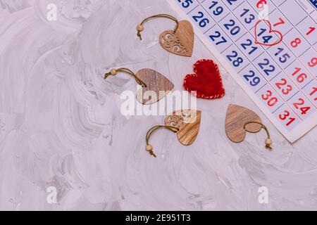 Blatt Wandkalender mit Datum Februar 14th markiert. Rotes Herz aus Wolle und viele Herzen aus Holz mit Ornamenten geschnitzt. Komposition für Vale Stockfoto