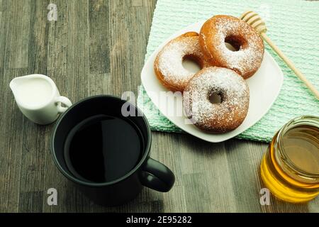 Donut und Kaffee mit Milch zum Frühstück. Donuts in Zucker auf einem weißen Teller mit einer Tasse heißem Getränk runden. Hintergrund mit leerem Platz für Text Stockfoto