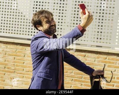 Junger kaukasischer Geschäftsmann nimmt ein Selfie auf der Straße mit Ein Elektroroller Stockfoto