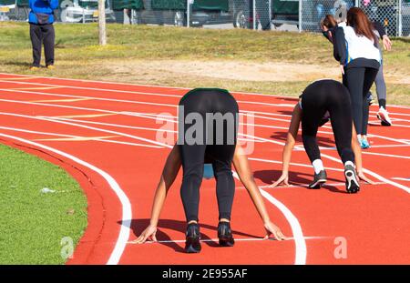 Rückansicht der weiblichen Sprinterläuferinnen in der eingestellten Position auf der Outdoor-Strecke während einer High-School-Strecke und Feld treffen mit Spandex. Stockfoto