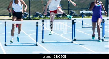 Drei High School Mädchen in einem vierhundert Meter Hürdenlauf auf einer Outdoor-Strecke im Sommer konkurrieren. Stockfoto