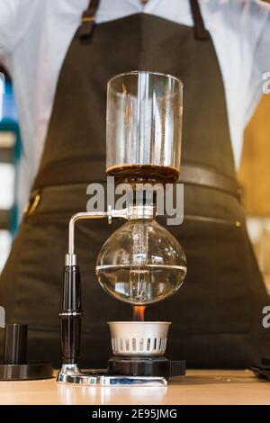 Kaffeebrühe mit Syphon Gerät. Nahaufnahme Siphon heizt durch Feuer. Brauen Foto auf dem Feuer. Alternative Methode der Kaffeeherstellung. Vertikales Foto fo Stockfoto