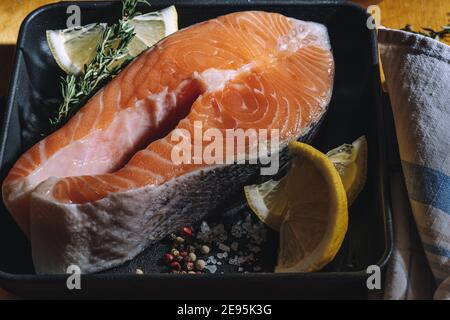 Rohes Lachssteak mit Zitrone und Thymian in gusseiserner Pfanne auf Holzboden. Raue Beleuchtung Stockfoto