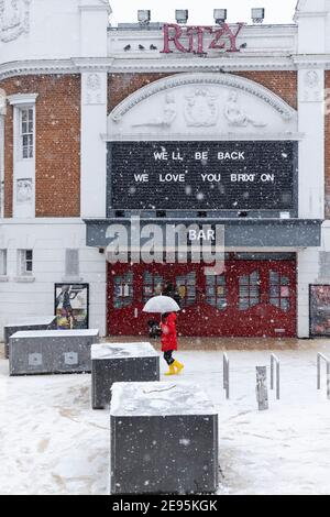 Eine Person mit Sonnenschirm läuft bei starkem Schnee am geschlossenen, ritzy Cinema vorbei, Windrush Square, Brixton, London, 24. Januar 2021 Stockfoto