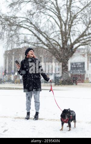 Ein junges Mädchen mit Hund lächelt bei starkem Schnee, Windrush Square, Brixton, London, 24. Januar 2021 Stockfoto